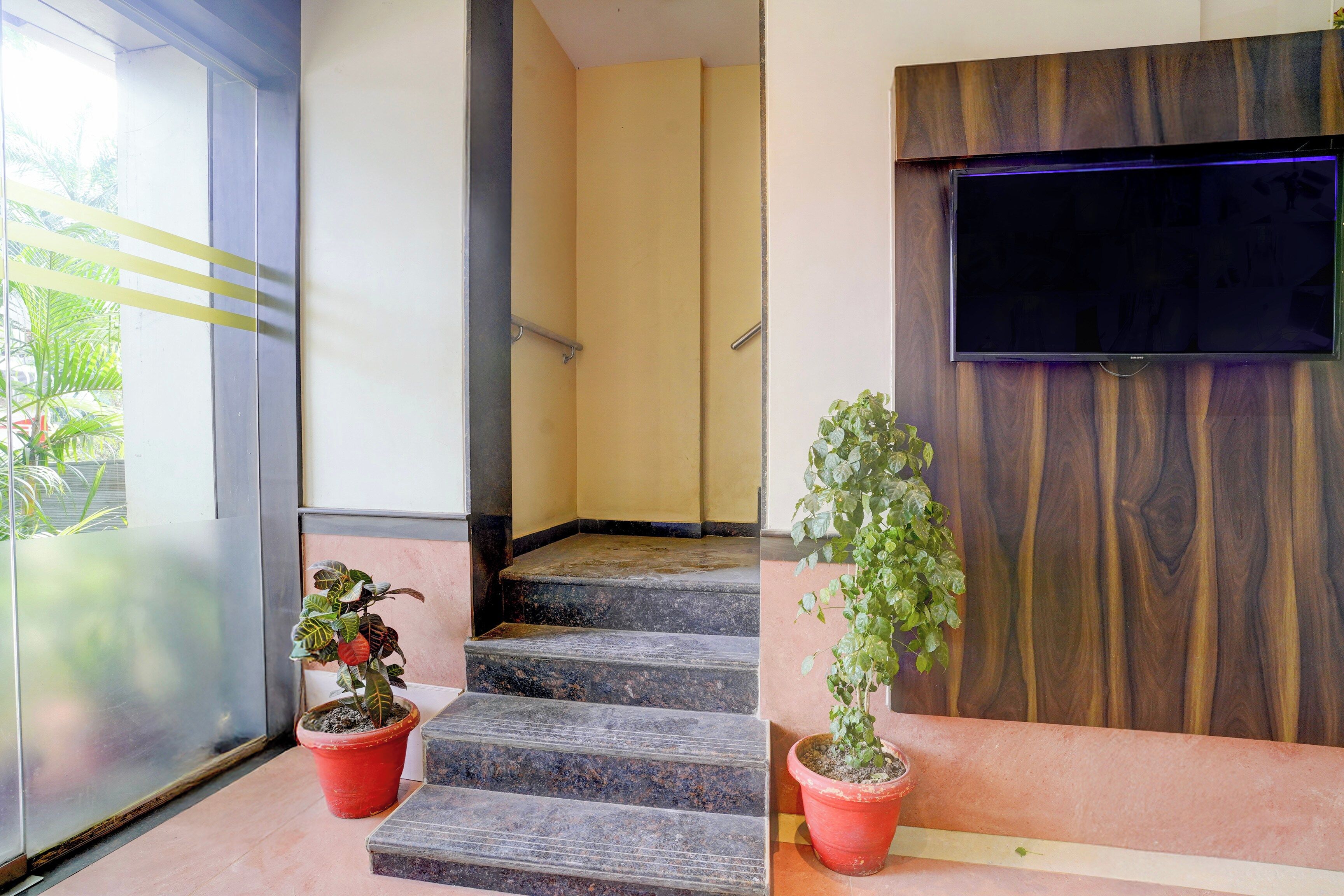 A staircase with a wooden finish, a flat-screen TV mounted on a wooden wall, and two potted plants on either side.