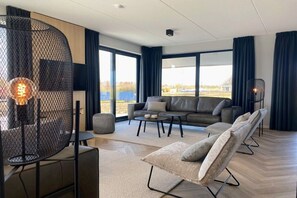 A modern living room with a sofa, coffee table, and chairs, large windows with curtains, and a unique light fixture. - Villa in Vrouwenpolder with Wifi (Vrouwenpolder)
