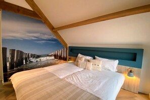 Une chambre à coucher avec un grand lit, une tête de lit et une fresque murale représentant un paysage côtier.