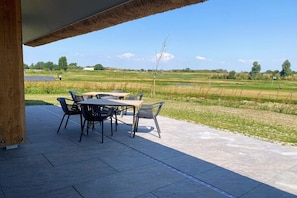 An outdoor patio with a table and chairs, a thatched roof, and a view of a green field. - Villa in Vrouwenpolder with Wifi (Vrouwenpolder)