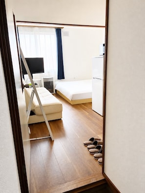 A compact room with a bed, a small desk, a television, and a refrigerator. - New Listing (小樽市)