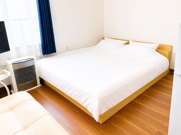 A hotel room with a single bed, a bedside table, a lamp, and a heater. - New Listing (小樽市)