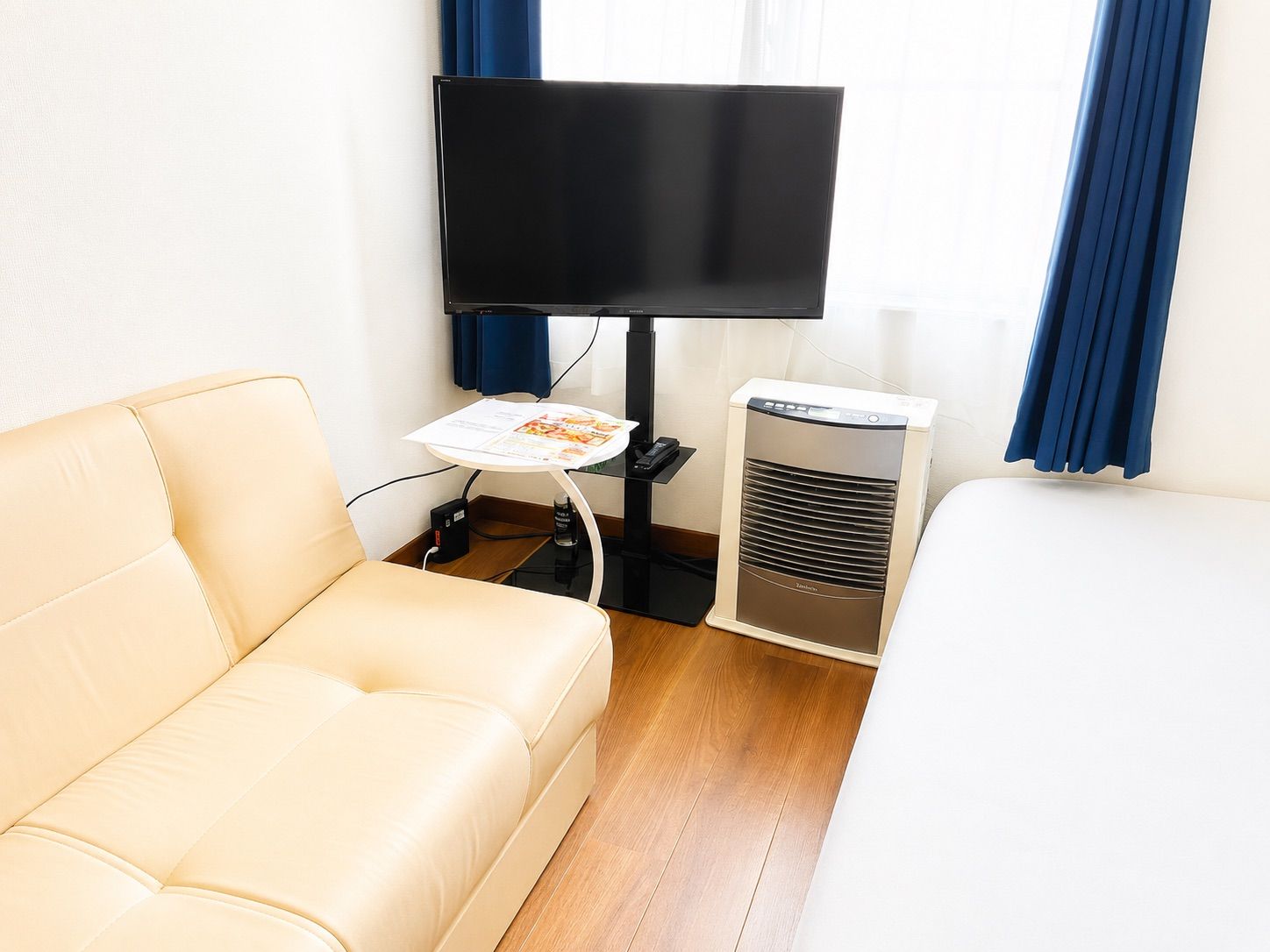 Een hotelkamer met een beige bank, een flatscreentelevisie, een klein tafeltje met een tijdschrift en een elektrische verwarming.