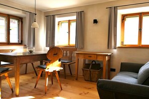 Ein Zimmer mit einem Holztisch, Stühlen, einer Couch und einem Fenster mit Vorhängen.