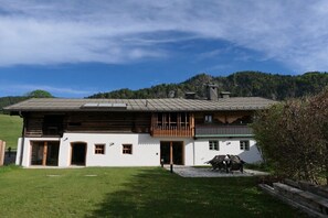 Un chalet à deux étages doté d’un balcon, d’une cheminée en pierre et d’une cour gazonnée.
