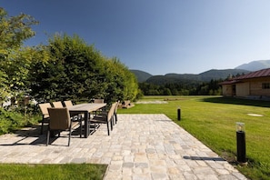 Une terrasse avec une table et des chaises en pierre, entourée d’une pelouse verdoyante et offrant une vue sur les montagnes.