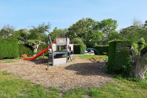 A playground with a slide and climbing structures, surrounded by well-maintained hedges and trees. - Holiday apartment with 1 bedroom (Zoutelande)