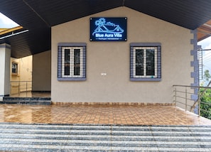 Ein Gebäudeeingang mit einem Schild, auf dem 'Blue Aura Villa' steht, und zwei Fenster mit Metallgittern.