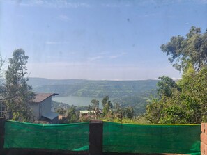 A view of a lake surrounded by hills, with a building in the foreground and a green netting barrier. - Beautiful 3-bedroom bungalow with AC in serene Panchgani (Panchgani, Satara)
