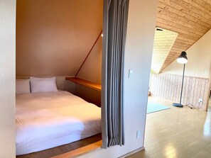 A bedroom with a sloped ceiling, a bed, a wooden shelf, and a floor lamp. - Mountain View Niseko 【Private Cottage with Great Views】 (ニセコ町)