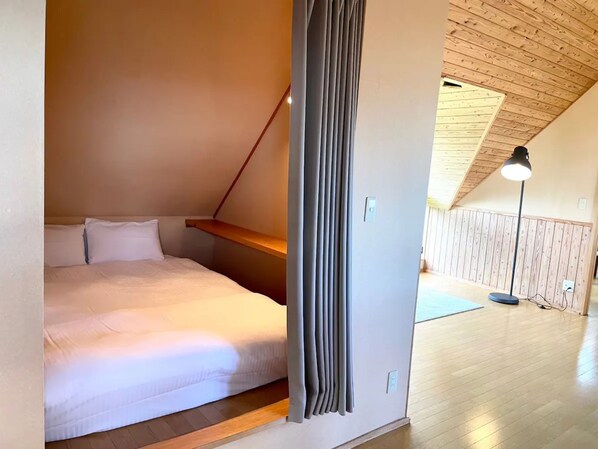 Ein Schlafzimmer mit schrägem Dach, einem Bett, einer Holzablage und einer Stehlampe.
