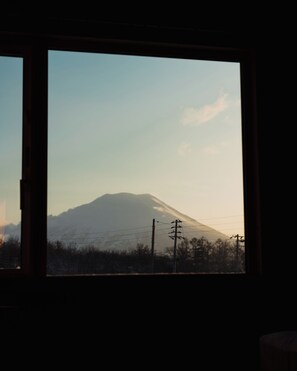 A window view of a mountain, possibly a volcano, with power lines and trees in the foreground. - Mountain View Niseko 【Private Cottage with Great Views】 (ニセコ町)