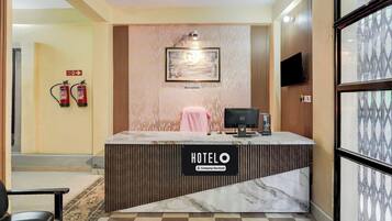 A hotel reception desk with a sign reading 'HOTELO Company Serviced', a framed picture above it, and a fire exit sign on the wall.