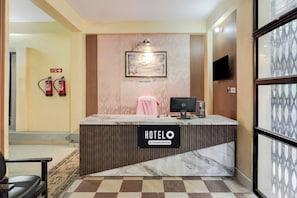 Ein Hotelrezeptionstresen mit einem Schild, auf dem 'HOTELO Company Serviced' steht, einem gerahmten Bild darüber und einem Notausgangsschild an der Wand.