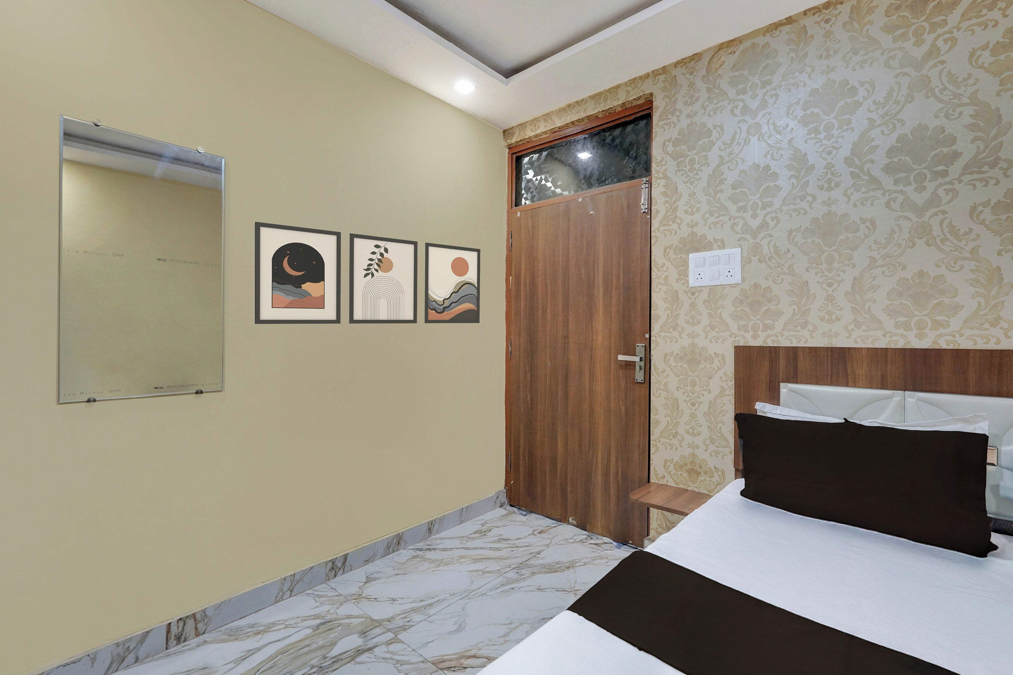 A hotel room with a bed, a door, and three framed pictures on the wall.