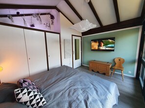 Quarto com cama, cómoda de madeira, televisão na parede e janela.
