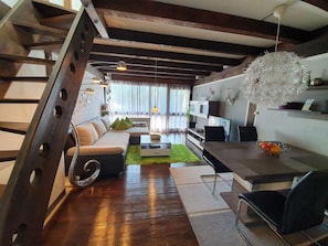 A modern living room with a staircase, a sofa, a coffee table, and a dining area with chairs. - Vacation Rental Between Chiemsee and Salzburg in the Pre-Alps *Wi-Fi, Thermomix, Balcony, View* (Siegsdorf)