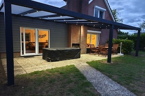 A covered patio area with a grill, outdoor seating, and a house with a brick facade. - Holiday home with 4 bedrooms (Bruinisse)