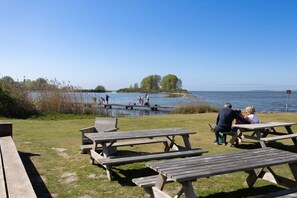 An outdoor seating area with picnic tables and benches overlooking a lake. - Holiday home with 4 bedrooms (Bruinisse)