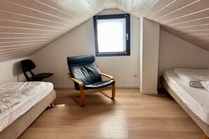 A small, sloped-roofed room with two beds, a single chair, and a window. - Bungalow with 3 bedrooms (Julianadorp)