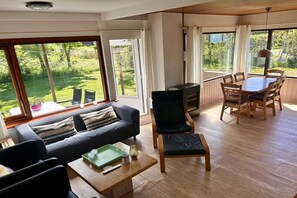 Un vaste espace de vie comprenant un canapé, une table à manger et des chaises. Une grande fenêtre offre une vue sur l’extérieur.