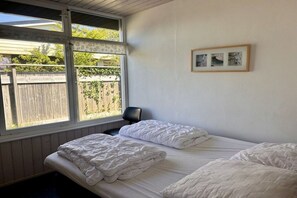 Une chambre avec deux lits, une fenêtre donnant sur une clôture en bois et un tableau encadré au mur.