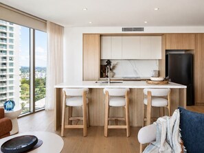 A modern kitchen with a central island, bar stools, and a large window offering a city view. - Elevated Escape at Sunrise - Lagoon Main Beach (Main Beach)