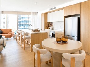 A modern kitchen with wooden cabinets, a central island, and a dining area with chairs. - Elevated Escape at Sunrise - Lagoon Main Beach (Main Beach)