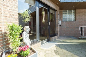 A building entrance with a brick facade, a glass door, and a small garden area with a statue and plants. - Holiday apartment in Issum with swimming pool (Issum)