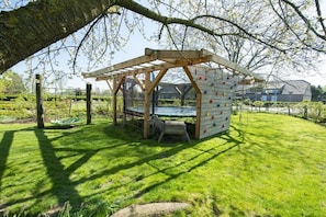 A wooden climbing structure with a swing, set in a grassy outdoor area with trees and a building in the background. - Holiday apartment in Issum with swimming pool (Issum)