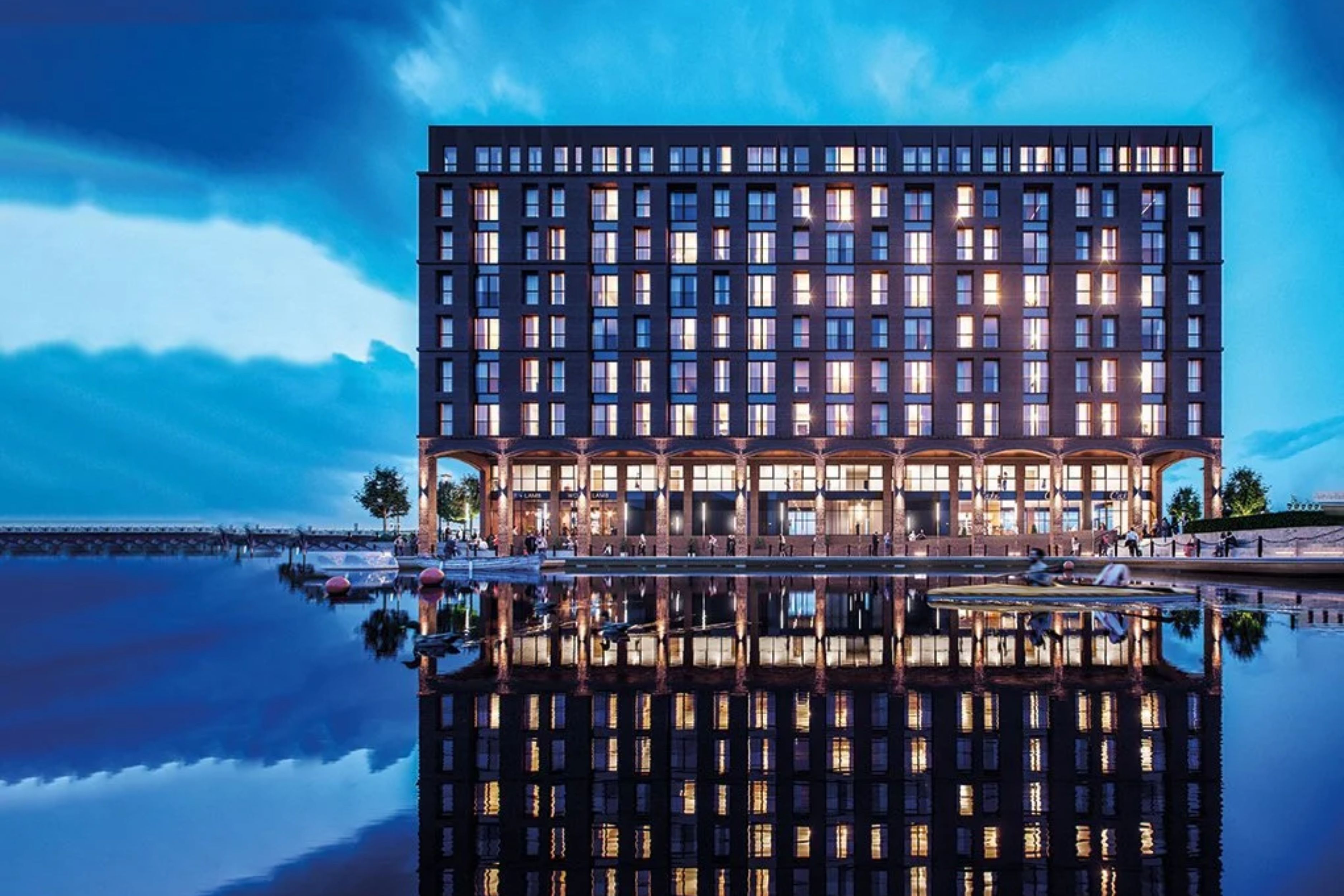 A modern hotel with a reflective pool in front, featuring a symmetrical facade with evenly spaced windows and a flat roof.