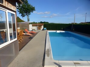 A swimming pool with a wooden deck and lounge chairs, a covered patio area, and a view of the surrounding landscape. - Holiday Home 'La Régordane' with Mountain View, Pool and Spa in Solignac-sur-Loire (Solignac-sur-Loire)
