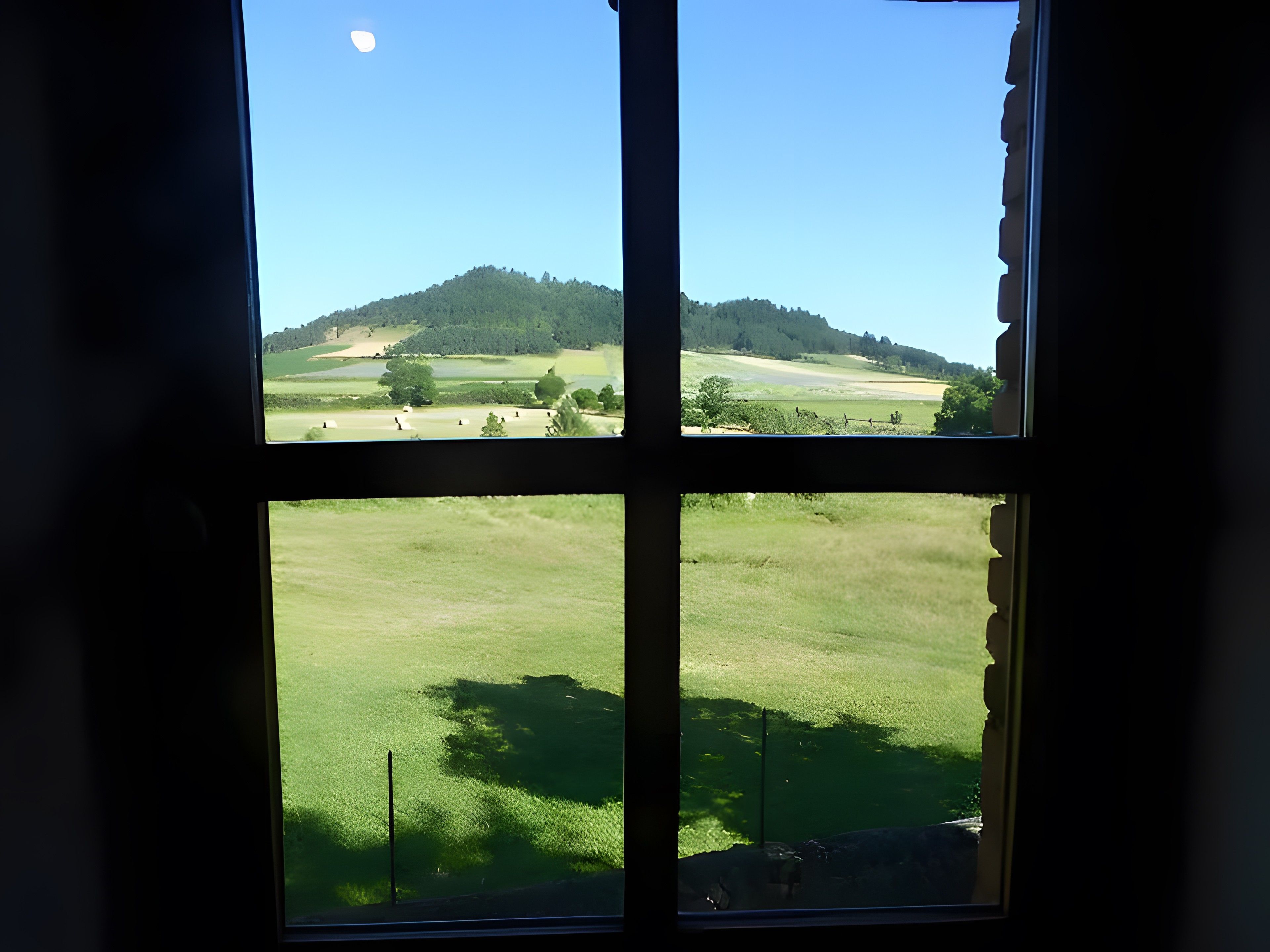 Una ventana con vistas a un campo verde y una colina.