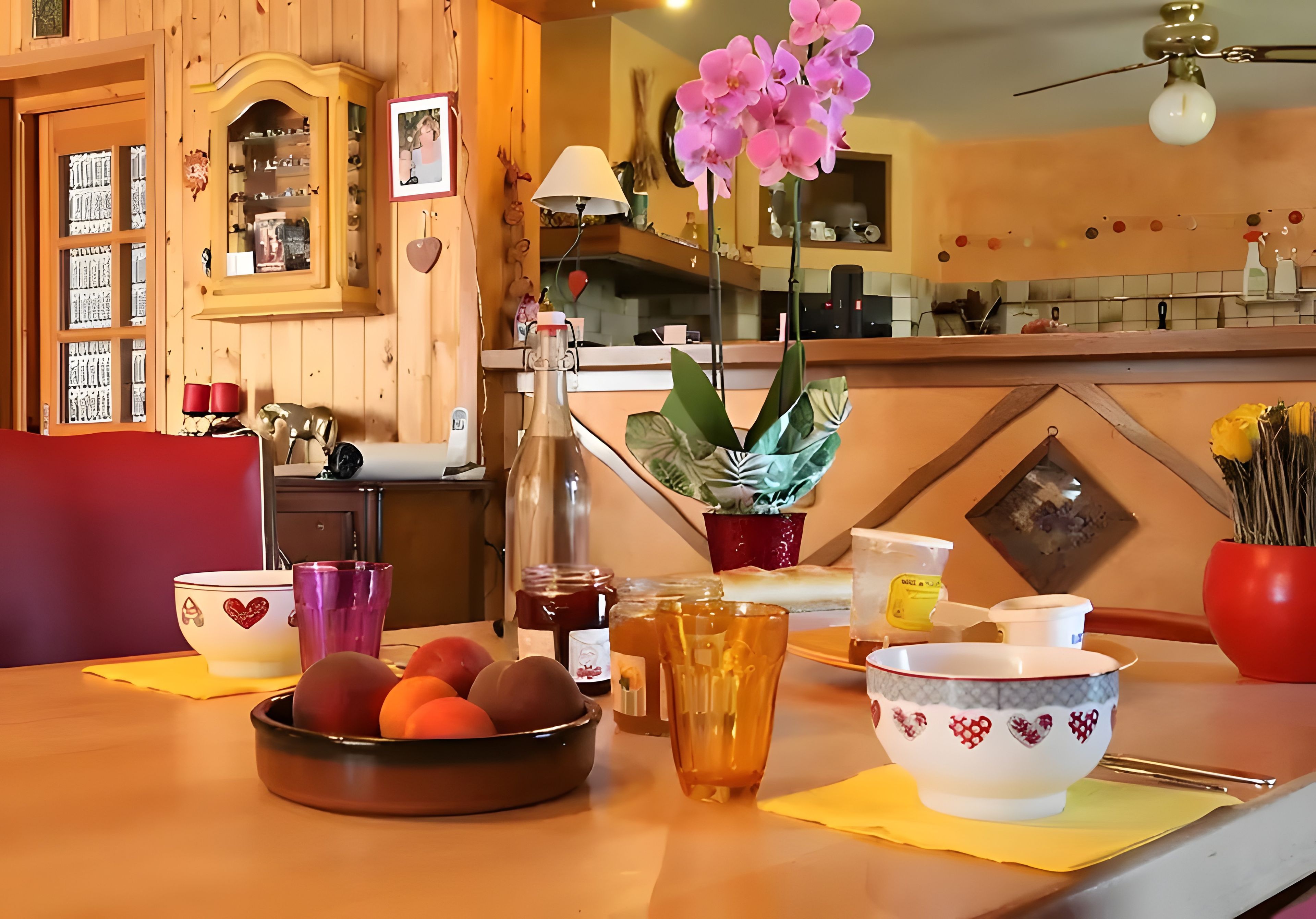 Een eethoek met een tafel gedekt voor twee personen, met een fruitschaal, een glas sap, een pot honing en een bloempot.