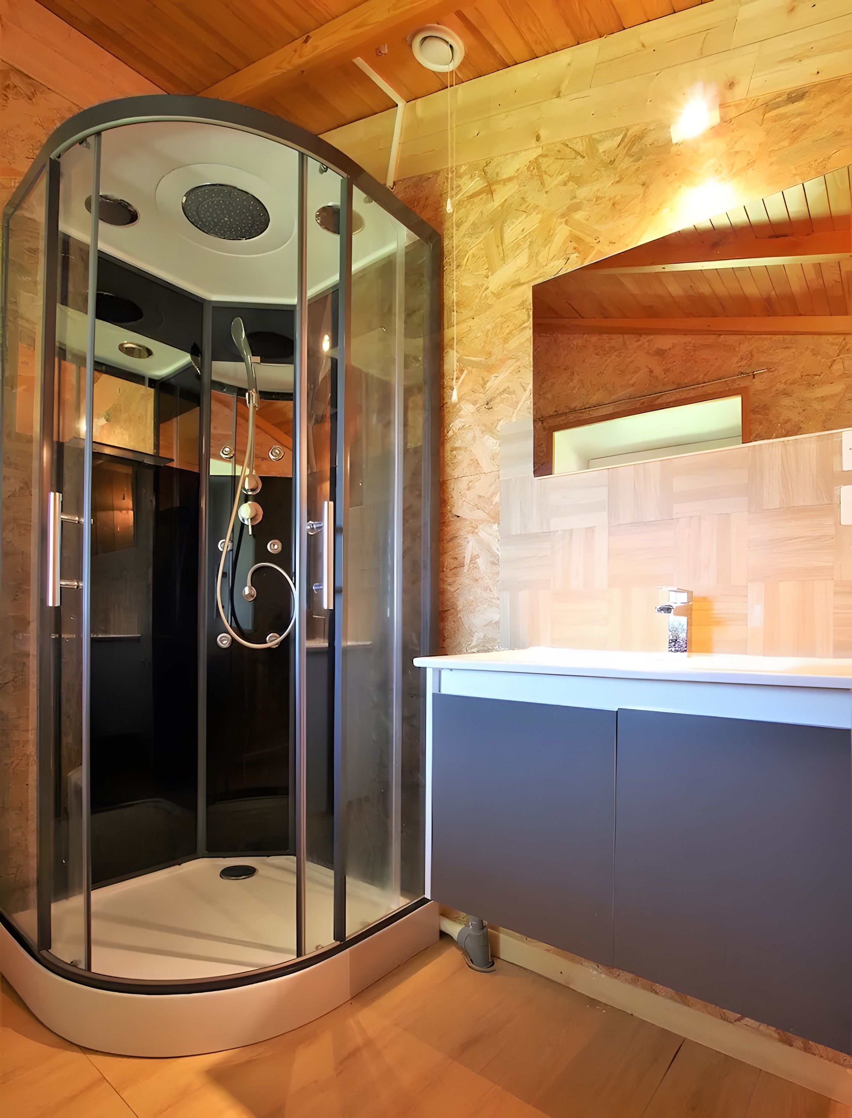 Un baño moderno con ducha acristalada, techo de madera y lavamanos empotrado con armarios.