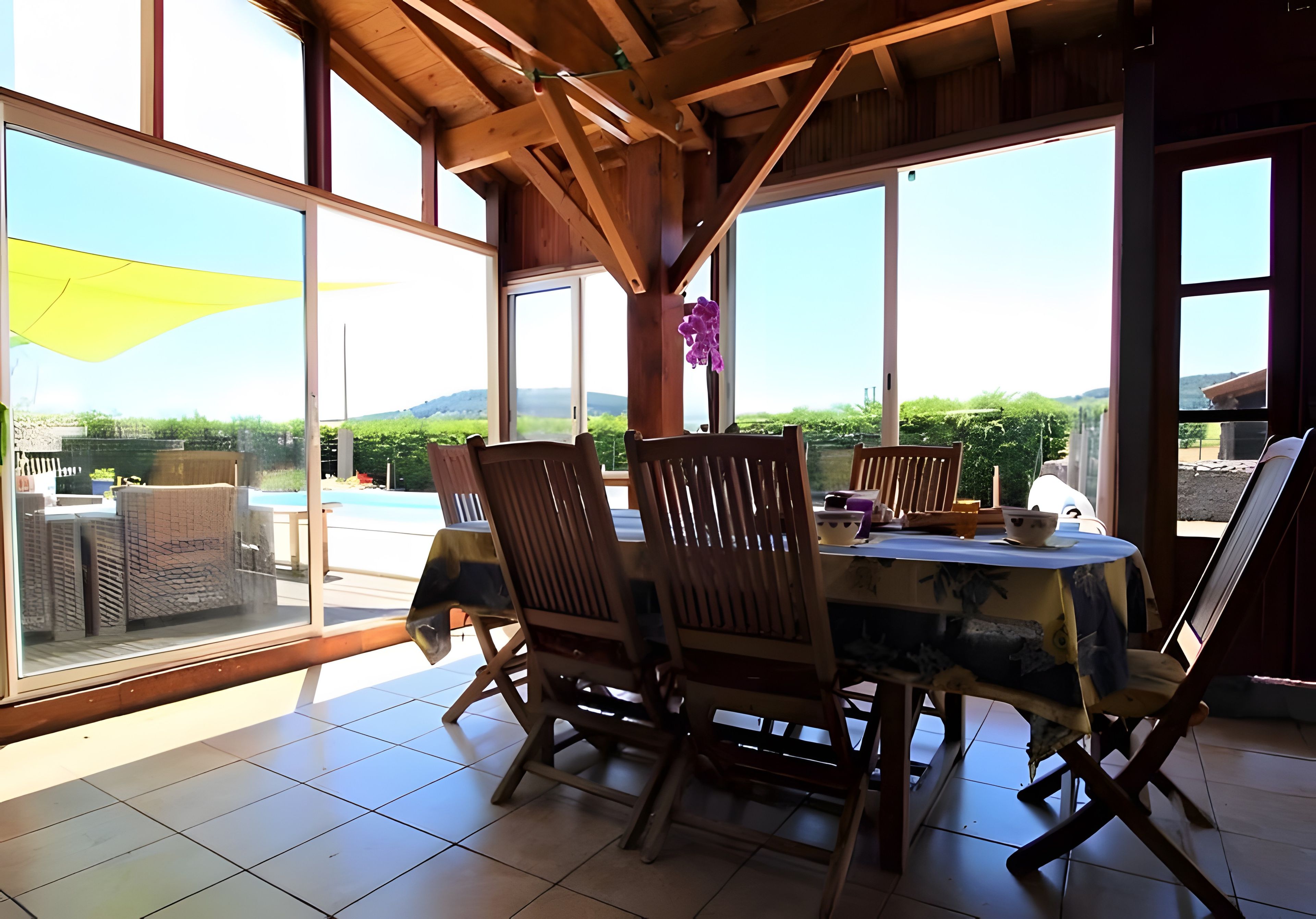 A dining area with a table, chairs, and a view of a swimming pool and greenery.