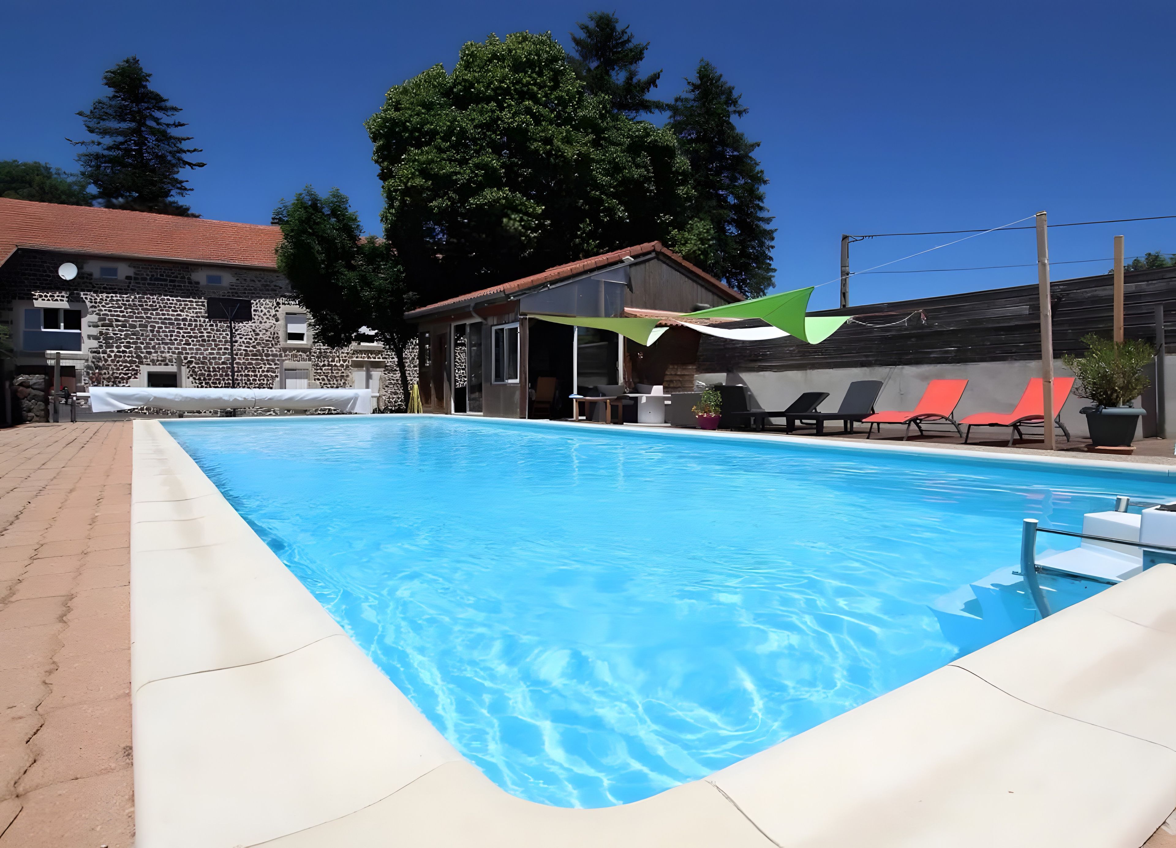 Una piscina con superficie de agua azul cristalina, rodeada de sillones de descanso y un edificio de piedra al fondo.