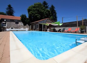 A swimming pool with a clear blue water surface, surrounded by lounge chairs and a stone building in the background.