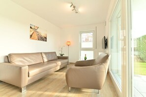 A modern living room with a beige sofa, a glass coffee table, and a floor lamp. - F in the holiday home TraumBlick (Lindau)