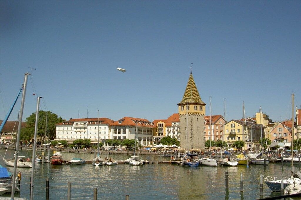 Een jachthaven met aangemeerde boten, een opvallende toren en gebouwen met rode daken.
