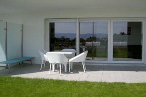 A patio area with a table and chairs, a bench, and a sliding glass door leading to a view of a landscape. - F in the holiday home TraumBlick (Lindau)