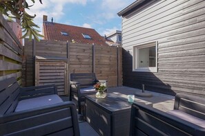 A patio with outdoor furniture, a wooden fence, and a house with a window. - Noordkerkepad Westkapelle (Westkapelle)