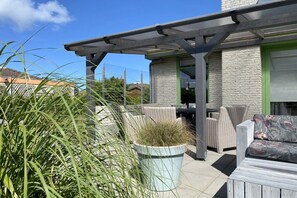 An outdoor patio with wicker furniture, a potted plant, and a pergola structure. - Holiday home with 3 bedrooms (Julianadorp)