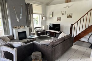 A living room with a fireplace, a television, a sofa, and a staircase. - Holiday home with 3 bedrooms (Julianadorp)