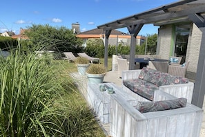 Eine Terrasse im Freien mit Korbmöbeln, einer Steinwand und einem Pergolen-Überbau.