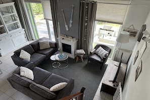 Ein Wohnzimmer mit Ecksofa, einem kleinen Tisch, einem Kamin und einem Essbereich mit Fernseher.