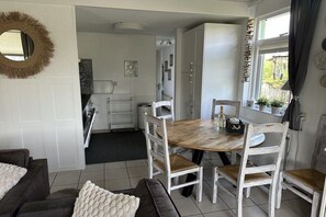 A dining area with a wooden table and white chairs, a kitchen in the background, and a mirror on the wall. - Holiday home with 3 bedrooms (Julianadorp)