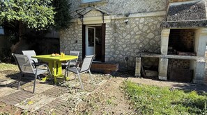 Eine Terrasse im Freien mit Tisch, Stühlen, einer Steinmauer und Grillplatz.