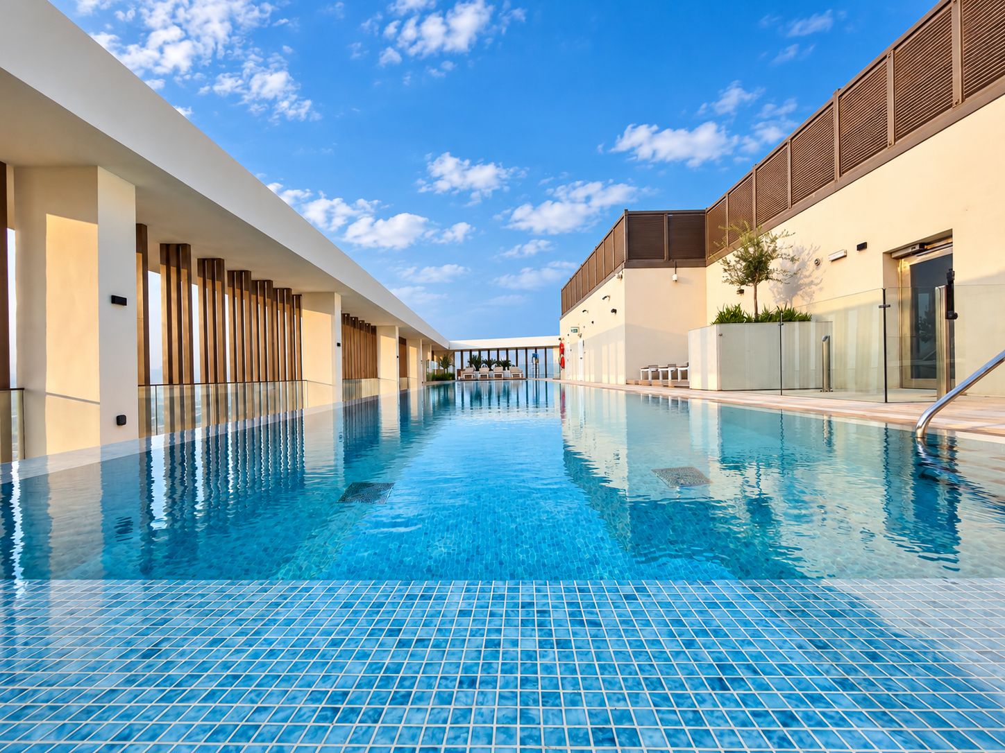 Una piscina con suelo de baldosas, rodeada por un edificio de diseño moderno y un cielo despejado.