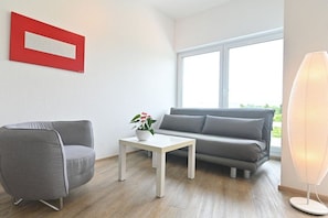 A modern living room with a grey sofa, a grey armchair, a white coffee table, and a floor lamp. - Holiday apartment with 1 bedroom (Lindau)